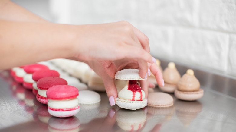 A hand places the top onto a filled macaron