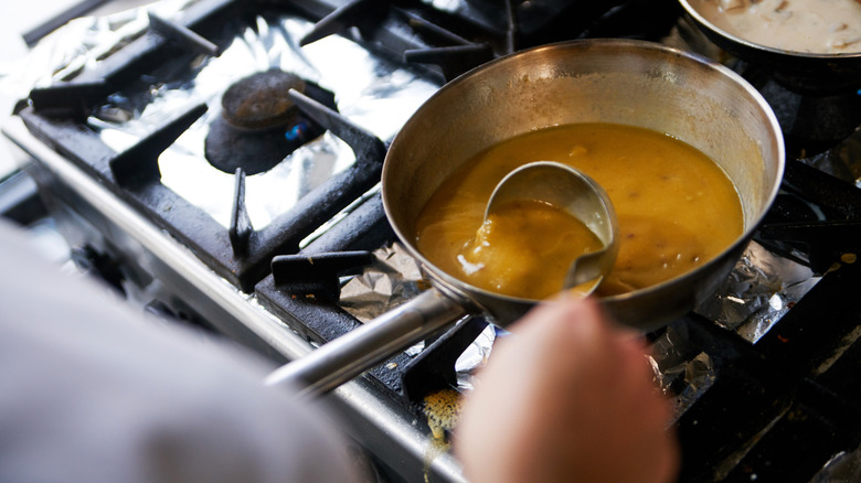 A cook stirring gravy on the stove