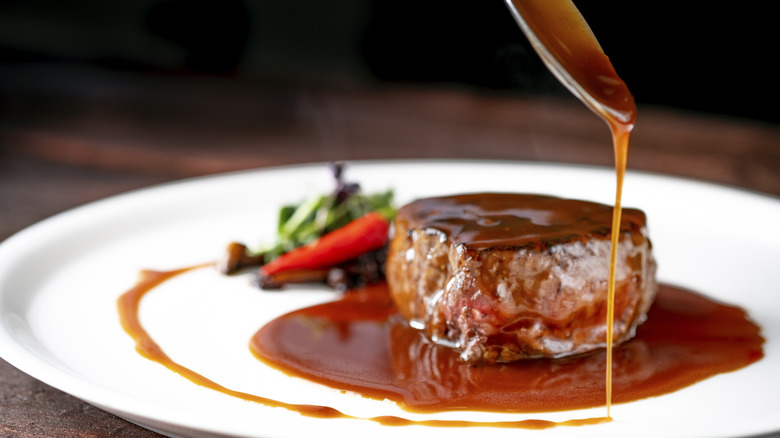 Demi-glace sauce being spooned over a steak