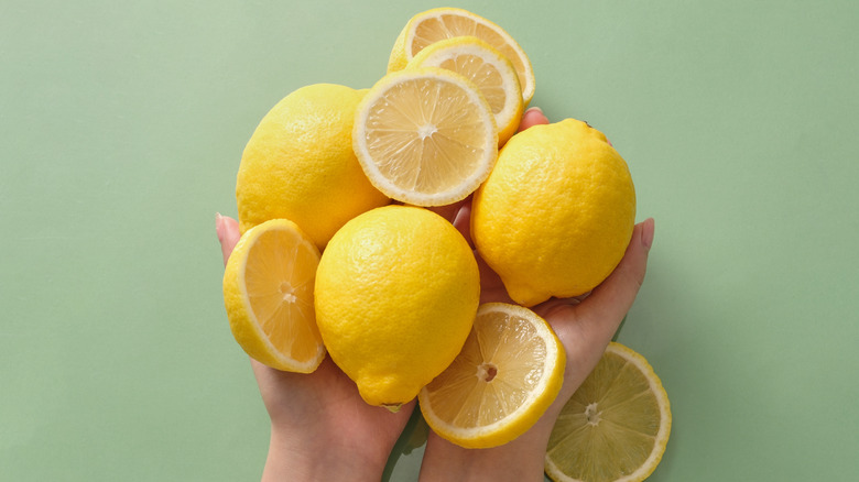 Person holding whole and sliced conventional lemons