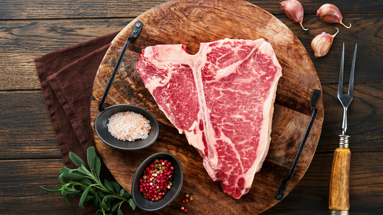 A large, thick steak on a board with spices