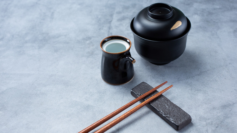 A set of chopsticks resting on a stand with a small pitcher and covered bowl sitting next to them