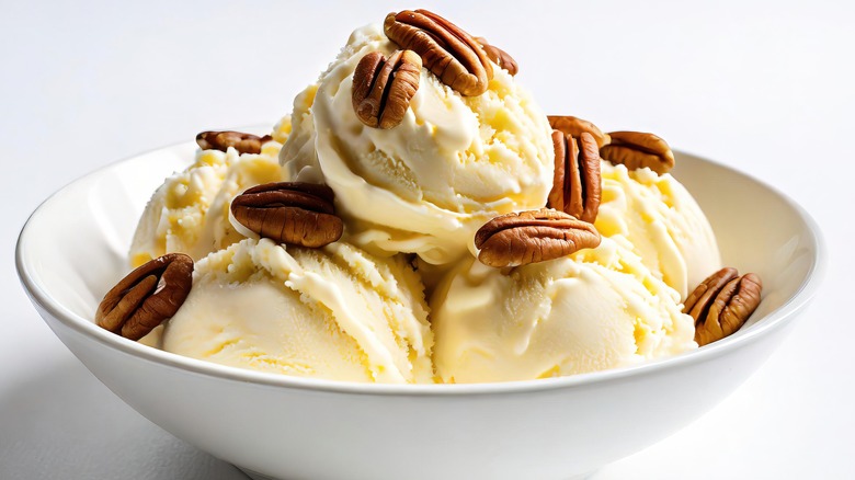 A bowl of butter pecan ice cream with pecans scattered on top