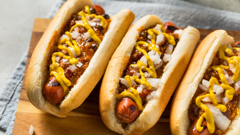 Three Coney Island hot dogs with chili, mustard, and onions