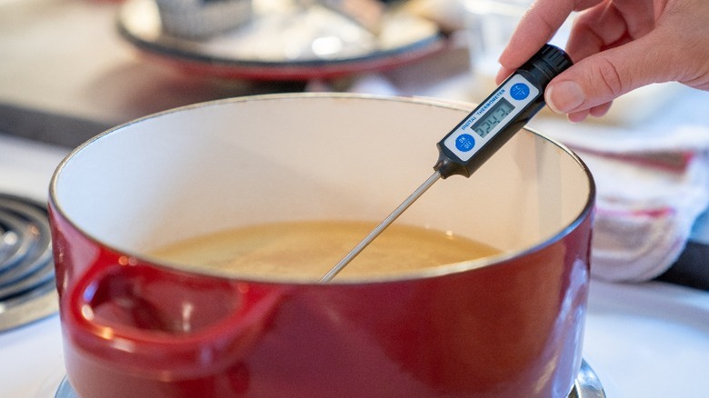 Person checking the temperature of fry oil in a Dutch oven