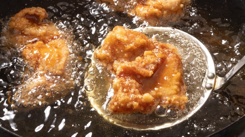 Fried chicken pieces submerged in bubbling oil