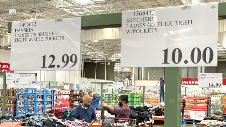 Costco price tags for clothing with people shopping in the background.
