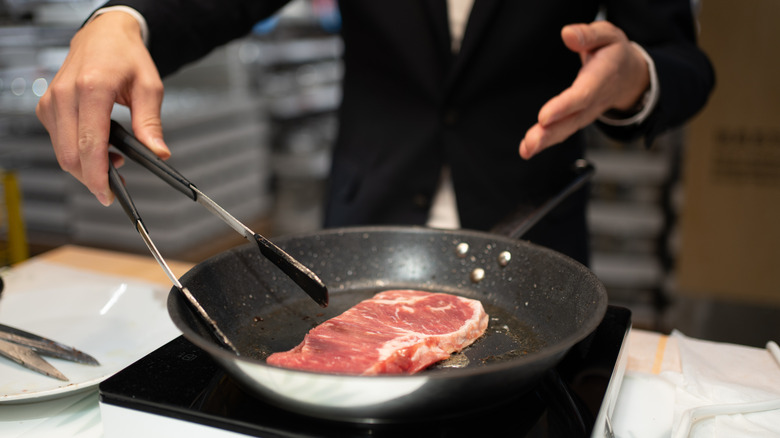 man frying steak in a pan