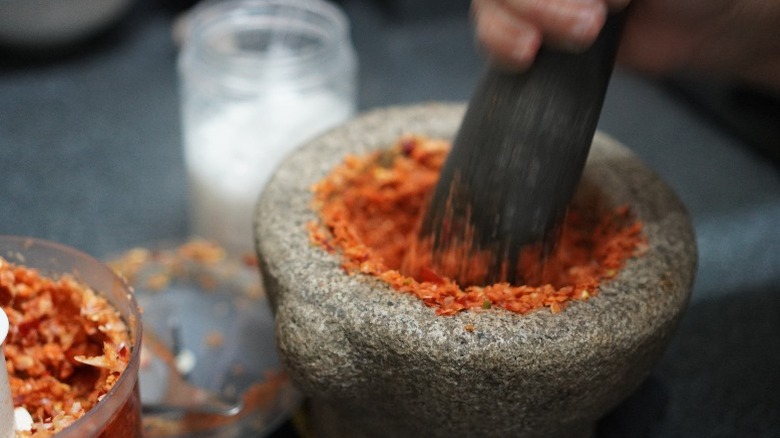Person uses a mortar and pestle to crush a variety of dried chiles and spices