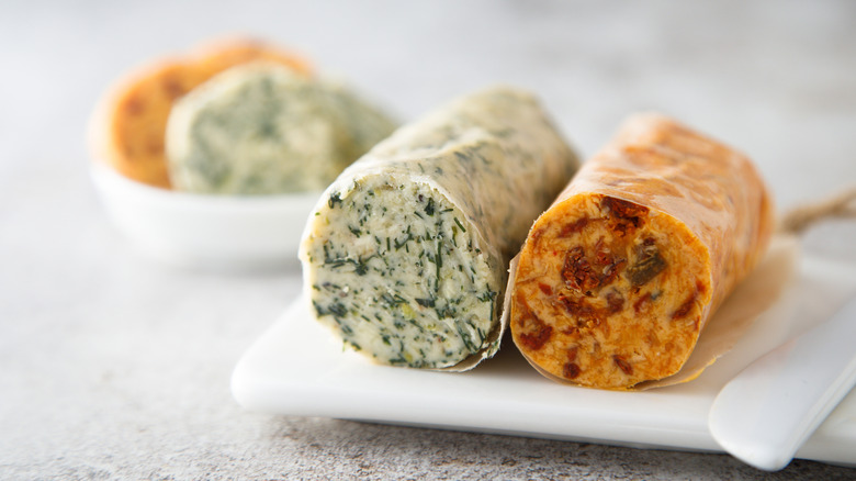 A light green tube of compound butter beside a reddish tube of compound butter on a plate.