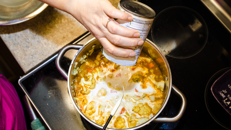 canned coconut milk poured into soup