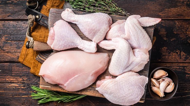 Raw chicken parts on a board againsts a wood background with garlic and herbs