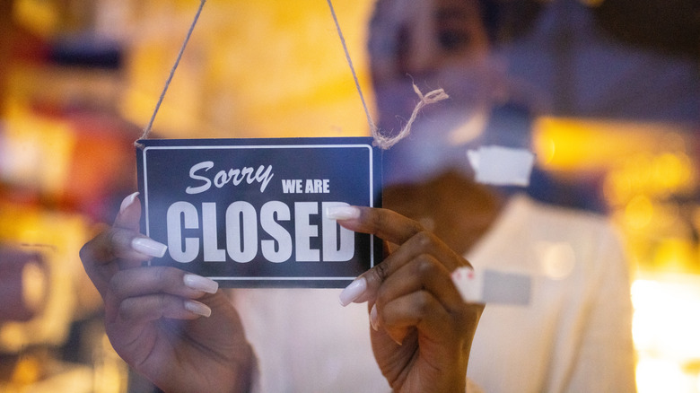 Woman putting up a sign that reads "Sorry we are closed"