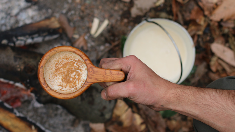 Guksi, a hand-carved burled mug, with coffee next to a pail of milk