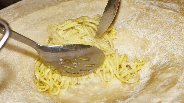 pasta stirred in cheese wheel with serving utensils