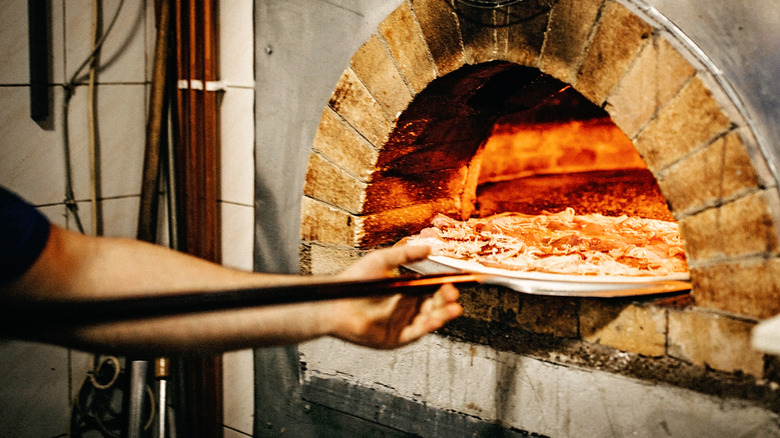 man putting pizza in oven 