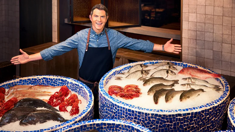 Bobby Flay in front of containers of iced seafood.