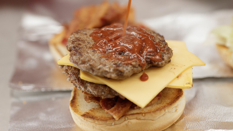 Five Guys bacon cheeseburger being squirted with ketchup