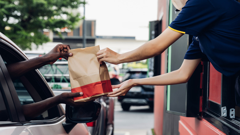 A person handing a bag of fast food to another person in a car.