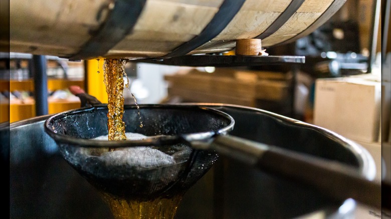 Whiskey pouring out of barrel and into sieve