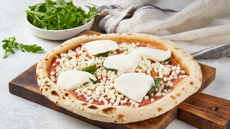 Raw frozen pizza on wood block with bowl of basil