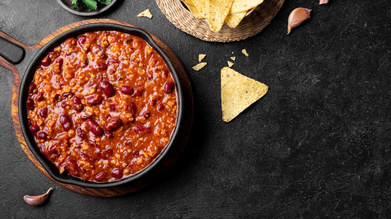 chili in a cast iron skilled on a black table next to tortilla chips