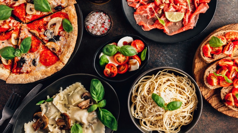 An assortment of Italian dishes: Neapolitan pizza, caprese, bruschetta, meats, and pastas on black serving plates