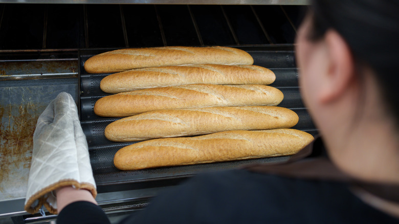 Woman pulling baguettes from oven
