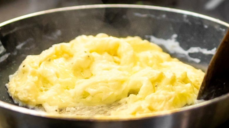 Wooden spoon stirring fluffy scrambled eggs in a pan