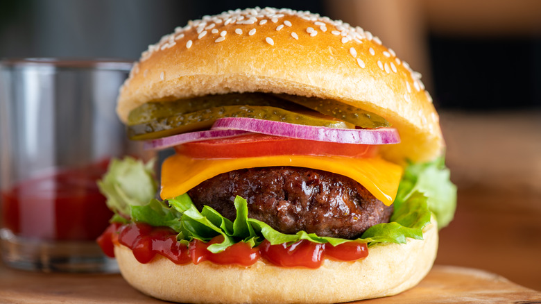 A juicy burger with ketchup, lettuce, cheese, tomato, onion, and pickles on a sesame seed bun.