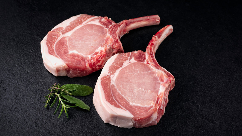 Bone-in pork chops are pictured with a sprig of herbs on a black background.