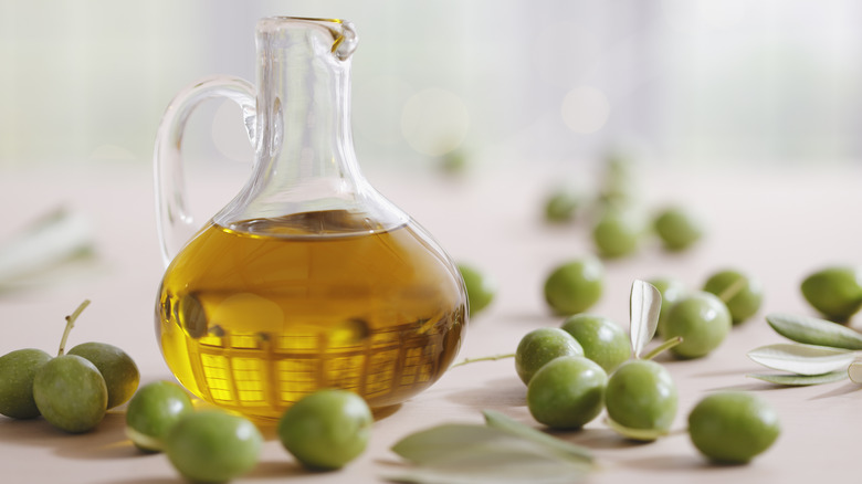 A glass carafe of olive oil surrounded by olives.