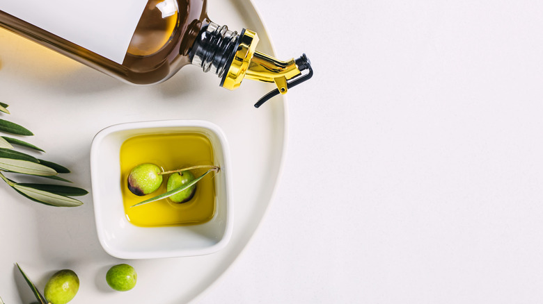 olive oil and green olives in a dish next to an olive oil bottle