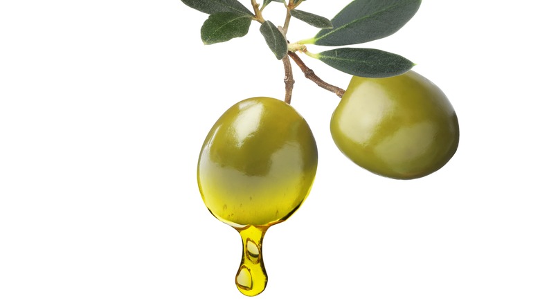 two green olives dripping oil against white background