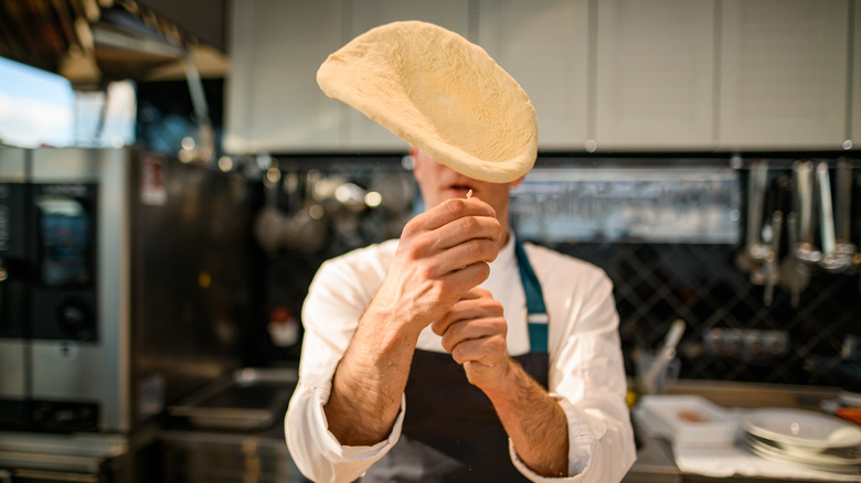 A chef hand-tossing pizza dough in a kitchen.