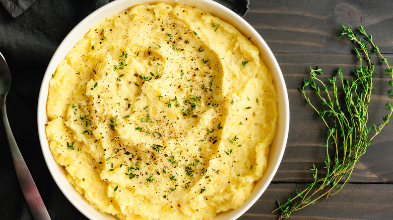 bowl of mashed potatoes with sprig of herbs on wooden table