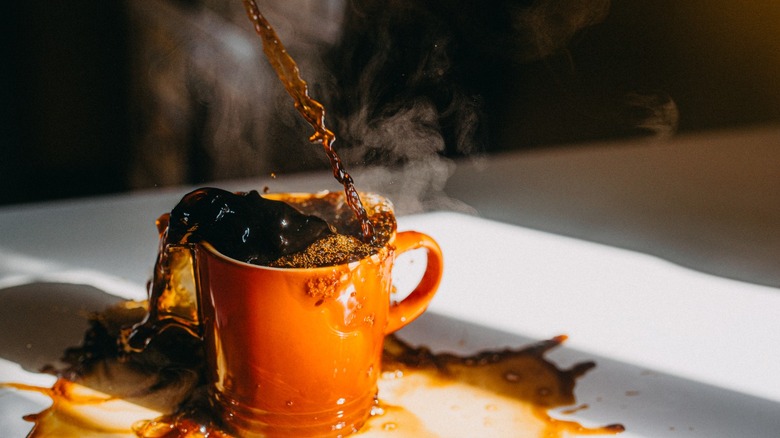 Coffee overflowing from a coffee mug spilling onto the table