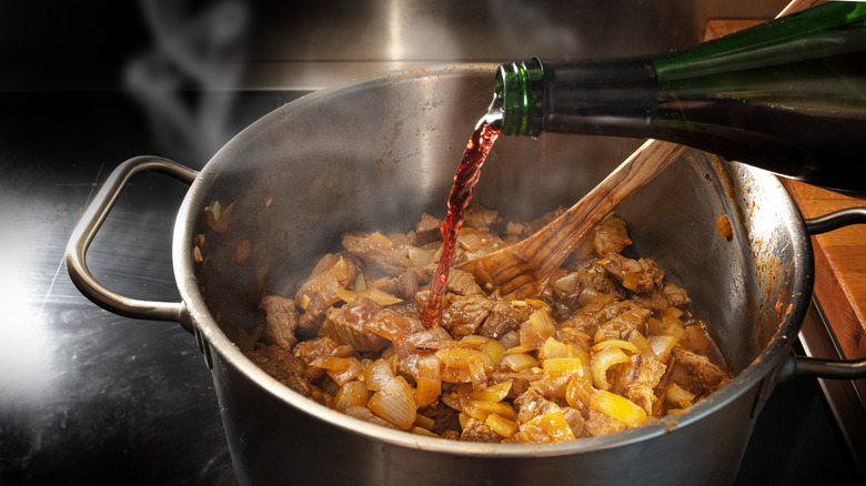 Red wine being poured into a meaty stew