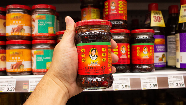 hand holding chili oil in front of Asian condiments at a store