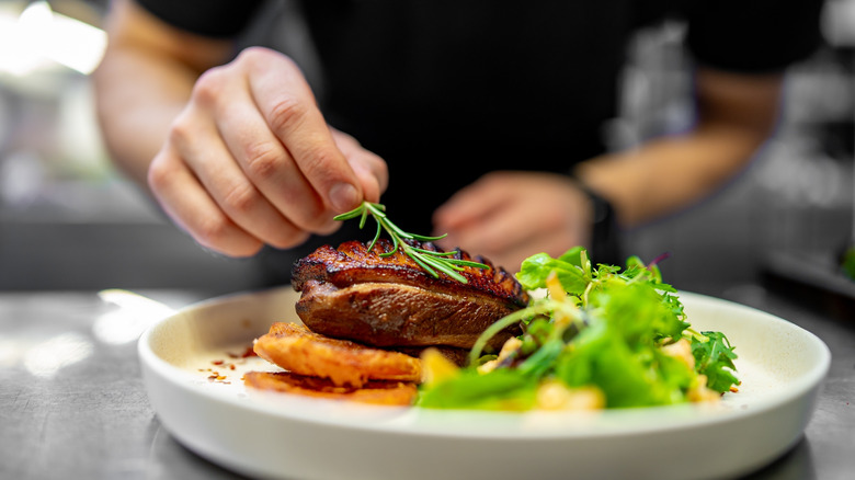 Chef adding herb garnish to meat dish