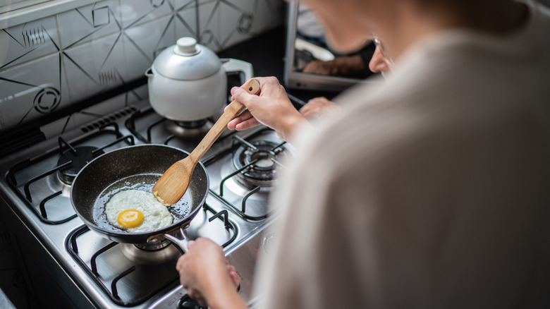 A person cooks a plain fried egg in a pan at home