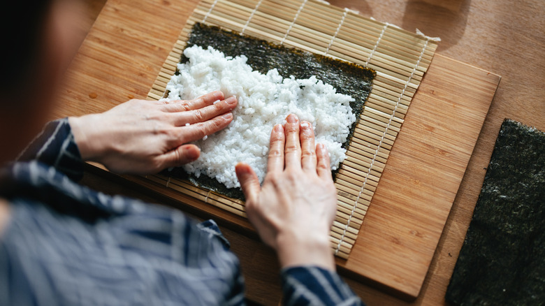 Hands spreading rice on nori