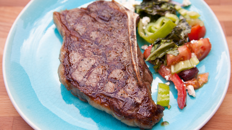 New York Strip steak with bone on blue plate and a side of vegetables