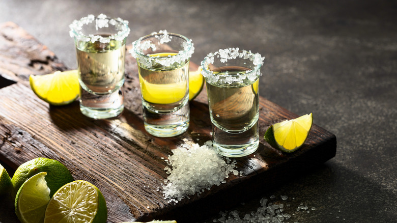 Three tequila shots with sea salt and lime wedges on a cutting board