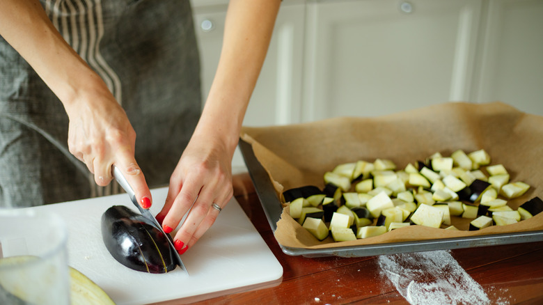 woman slicing and cubing eggplant on cutting board