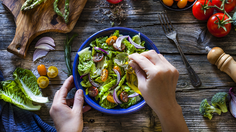 Hands pouring dressing onto a salad