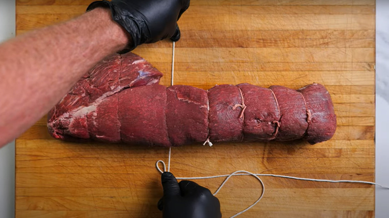 Hands tying beef tenderloin