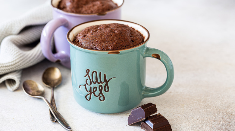 two chocolate mug cakes sitting on a white counter next to spoons