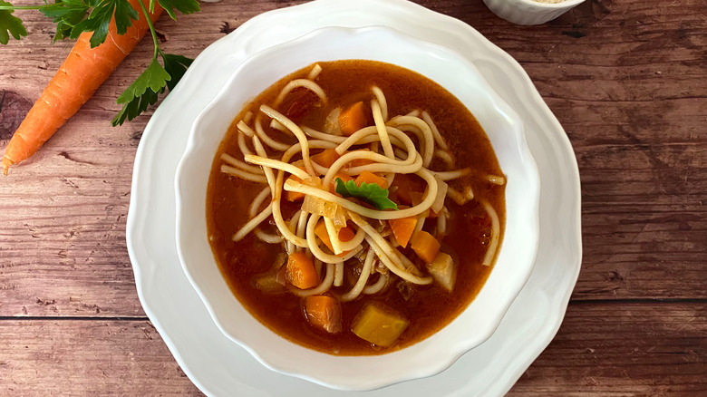 A bowl of minestrone soup with spaghetti in it.