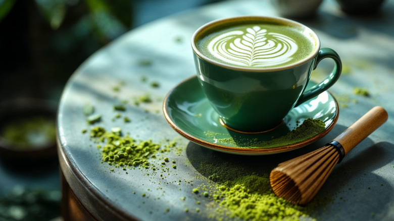 Matcha latte in a ceramic cup with matcha powder and a bamboo whisk